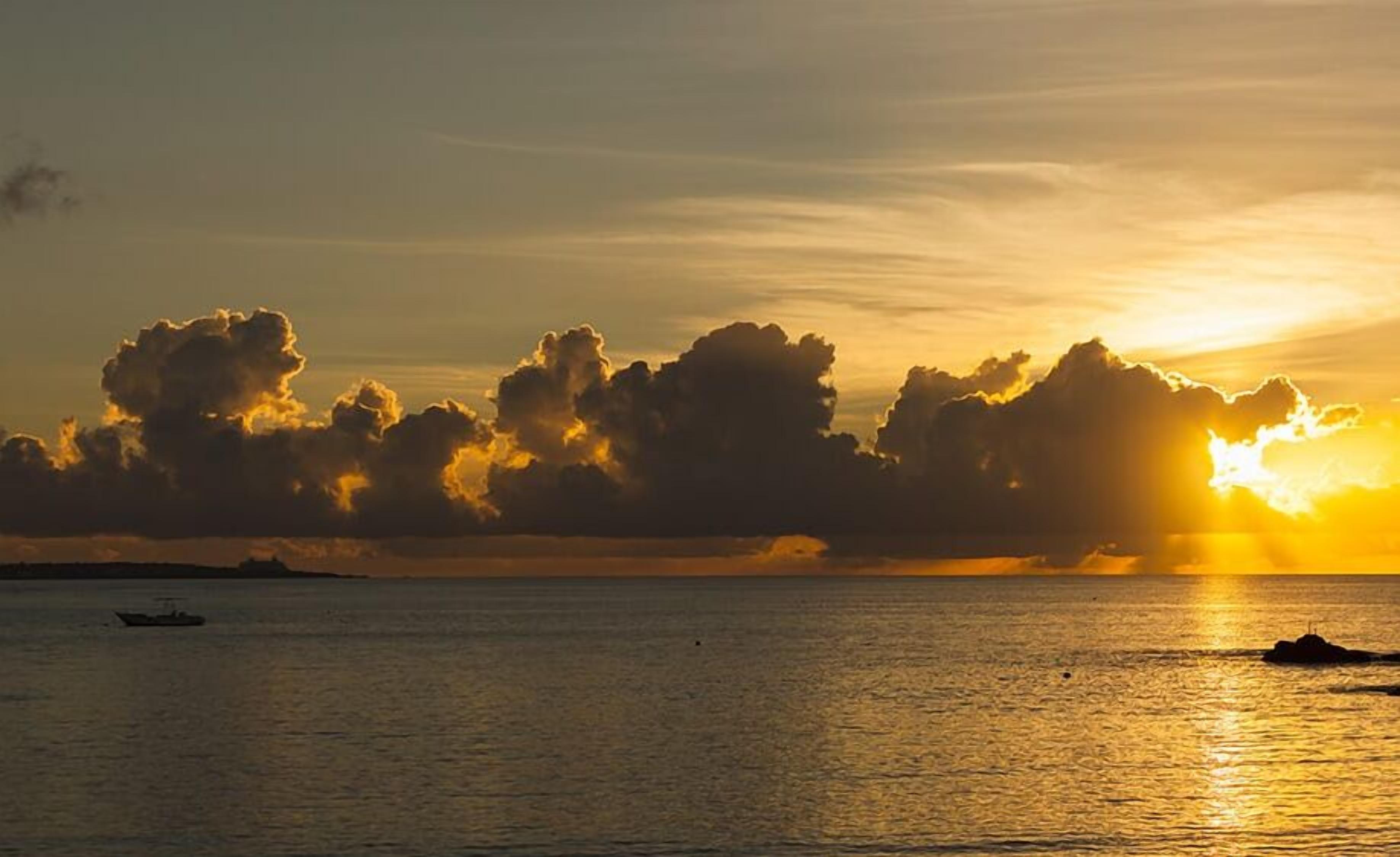 Un atardecer sobre un mar tranquilo con barcos y nubes.