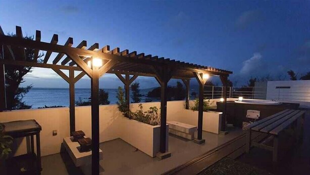 Une terrasse extérieure dotée d’une pergola, de sièges et offrant une vue sur l’océan au crépuscule.