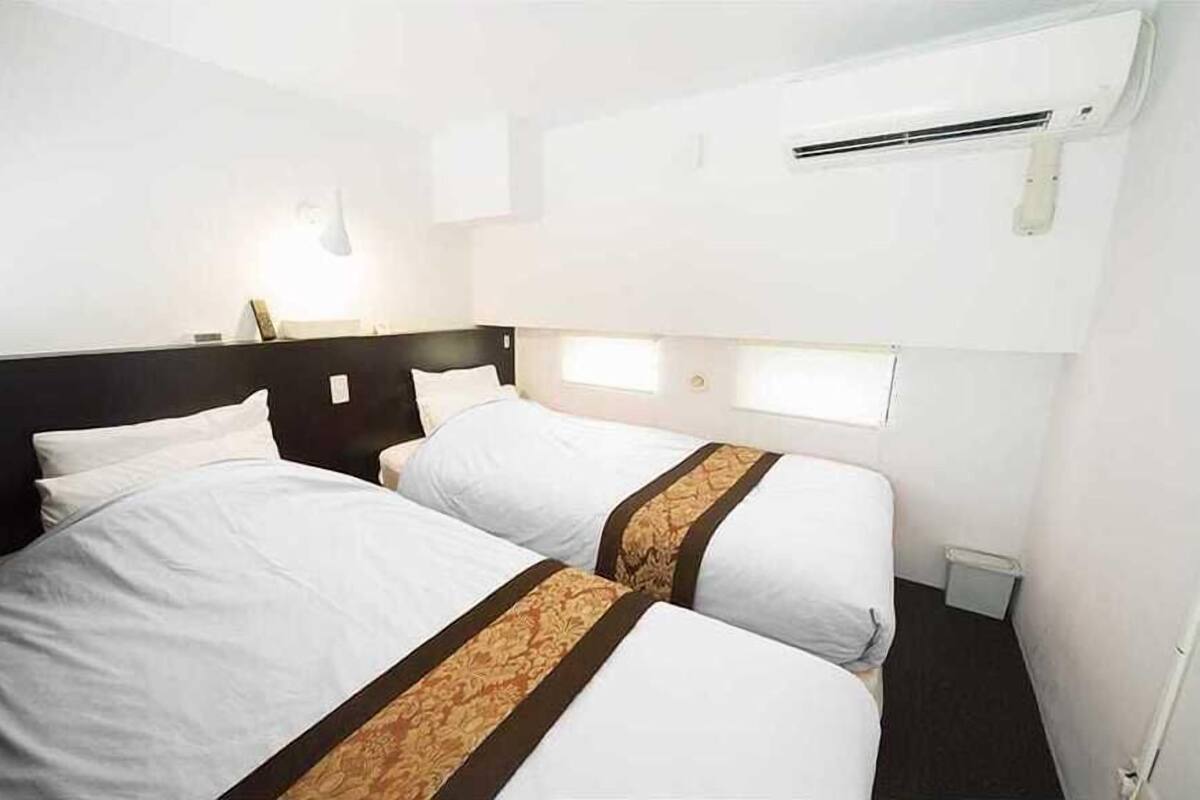 Una camera d'albergo con due letti, una finestra, un condizionatore e un comodino.