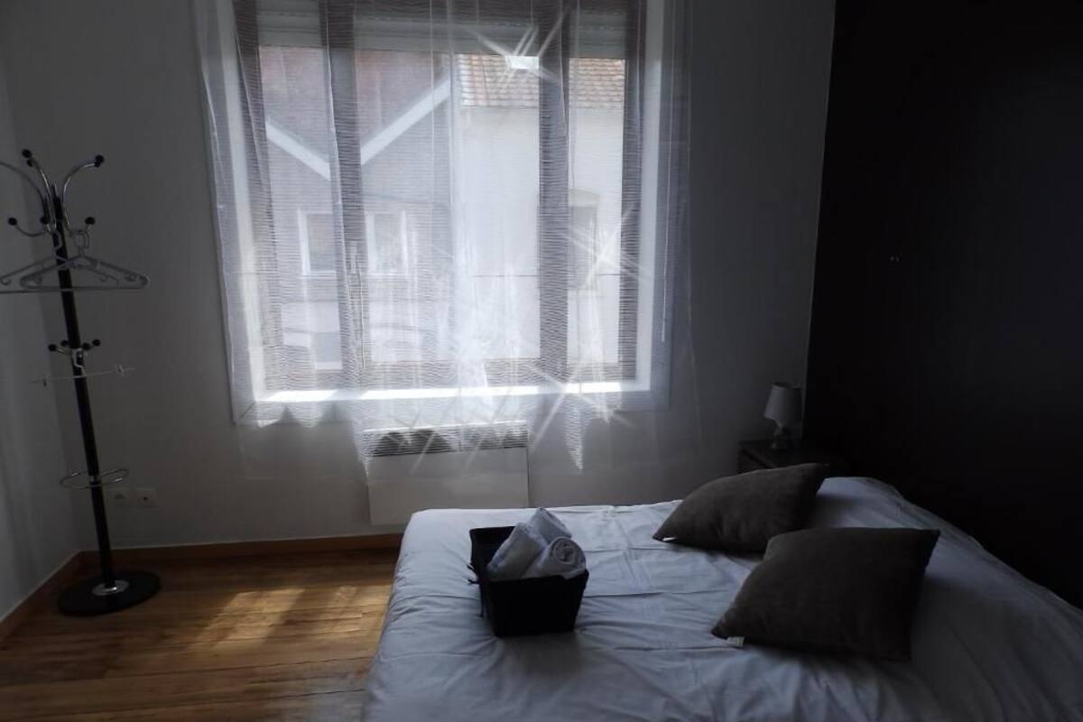 Ein Schlafzimmer mit Bett, Nachttisch, Fenster mit durchsichtigen Vorhängen und Stehlampe.