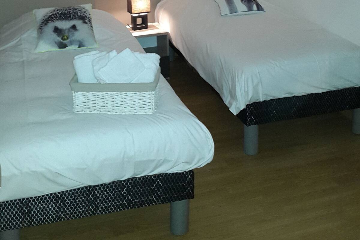 Ein Schlafzimmer mit zwei Betten, einem Nachttisch mit Lampe, einem Wandbild und einem Fenster mit Jalousien.