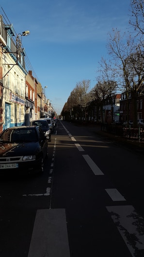 A street lined with parked cars and buildings, including a visible sign for a business. - Lens Louvre 2 (Lens)
