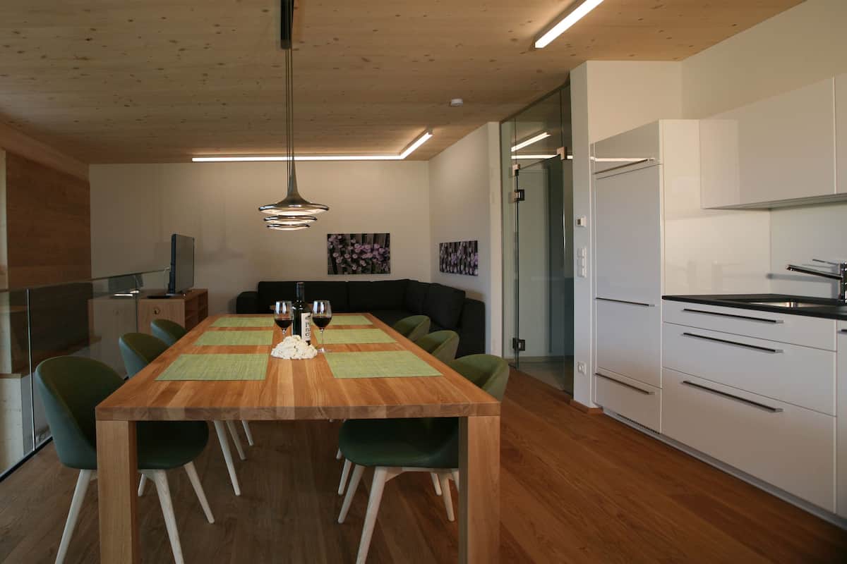 Cozinha moderna com mesa de madeira, cadeiras verdes e vista para montanhas através de grandes janelas.