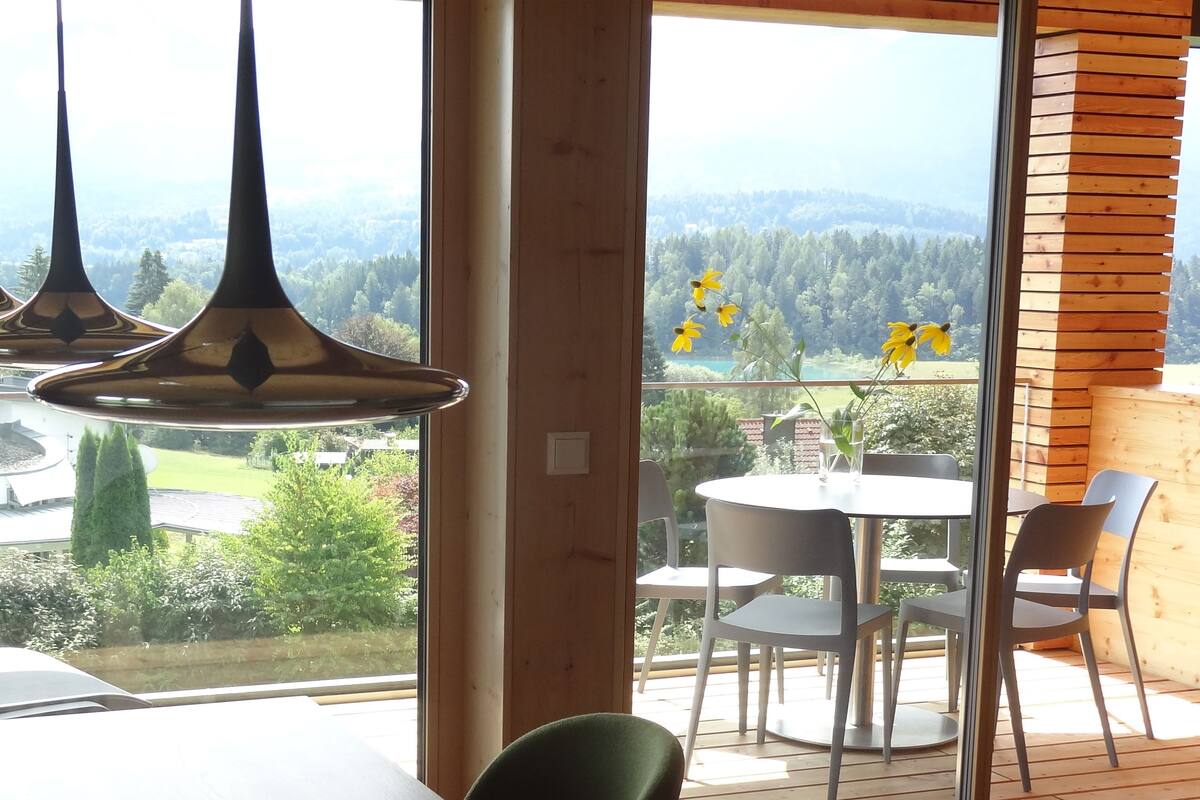 Quarto moderno com uma grande janela com vista para uma paisagem deslumbrante, uma mesa redonda com cadeiras e luminárias pendentes.
