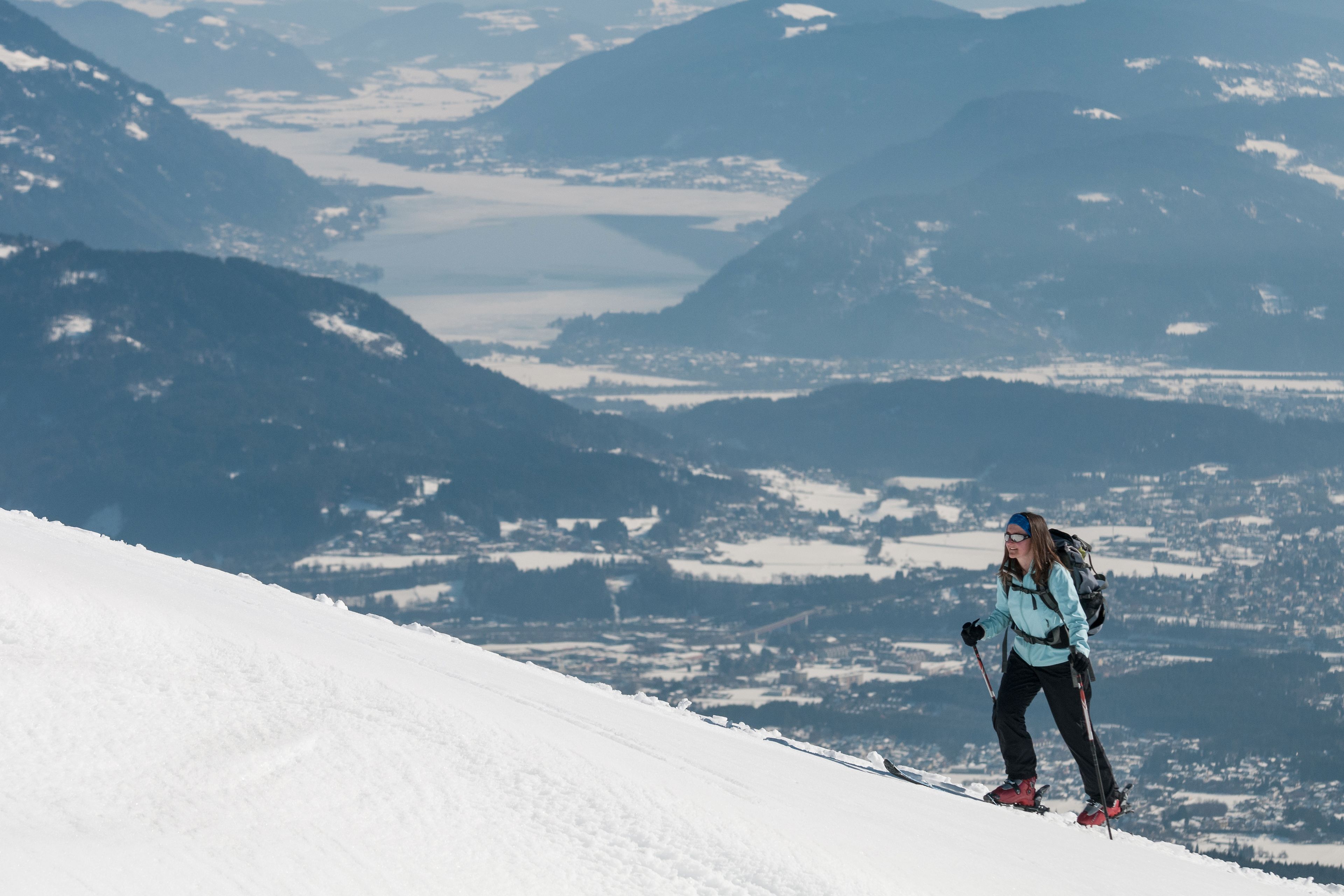 Une personne fait du ski sur une pente enneigée, avec un paysage montagneux en arrière-plan.