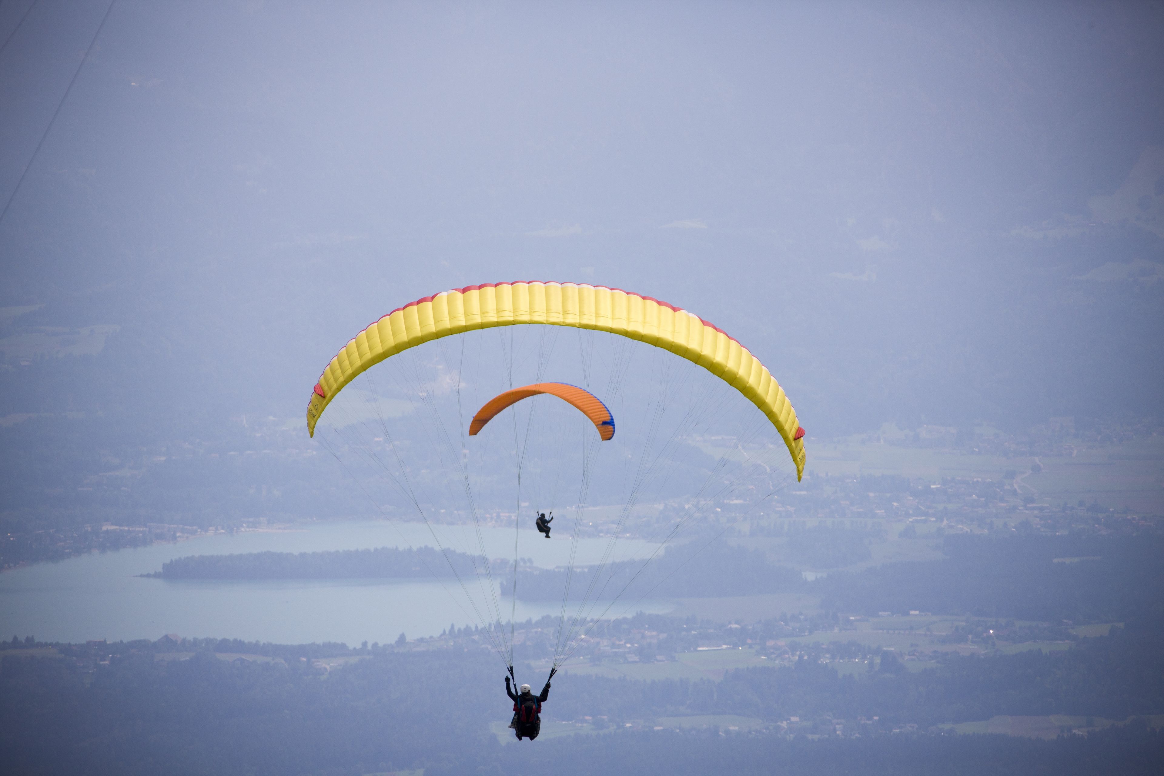 Twee paragliders met parachutes vliegen boven een landschap met een meer en heuvels.