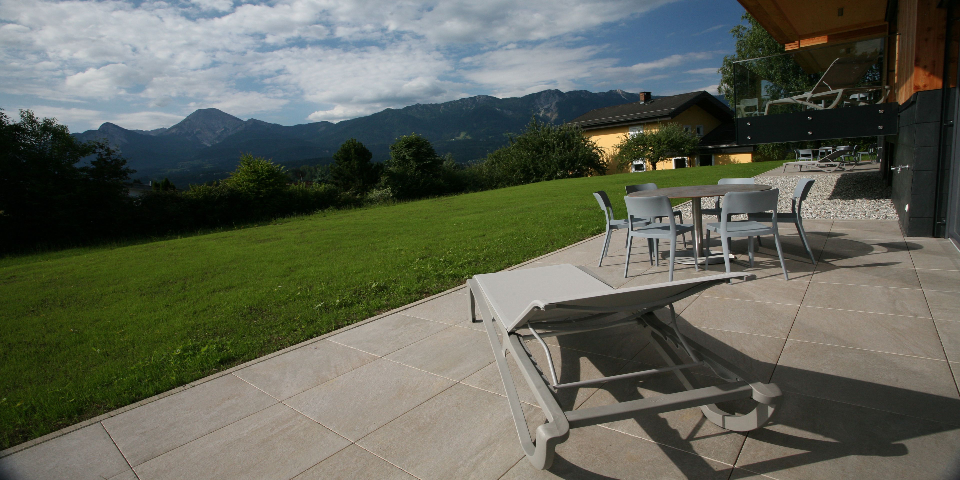 Une terrasse avec des meubles d’extérieur, une pelouse verdoyante et une vue sur les montagnes.
