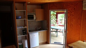 Une cuisine compacte équipée d’un four à micro-ondes, d’une machine à café et d’un petit réfrigérateur. On y trouve une table en bois et une porte donnant sur un espace extérieur.
