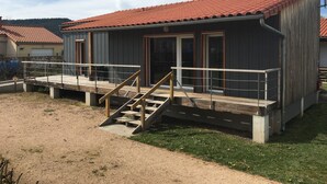 Un bâtiment avec un toit recouvert de tuiles rouges, une terrasse en bois et un escalier menant à une porte.
