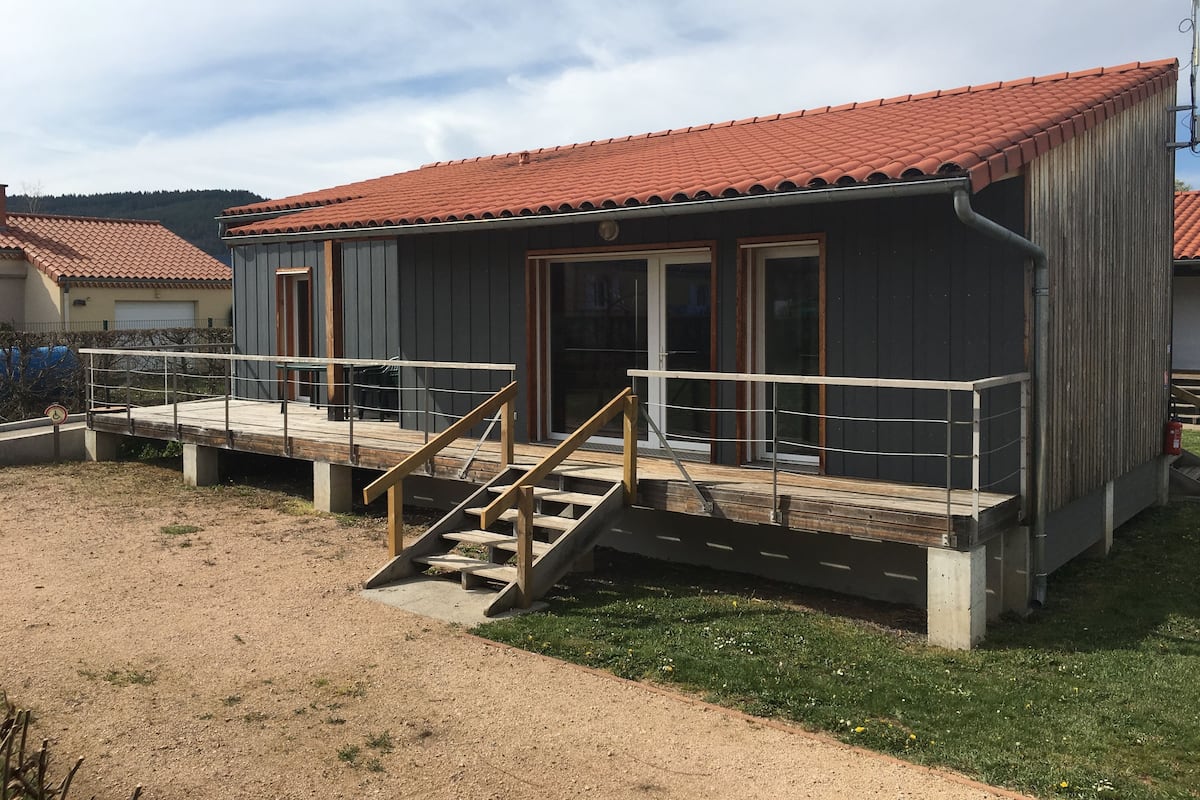 Un bâtiment avec un toit recouvert de tuiles rouges, une terrasse en bois et un escalier menant à une porte.