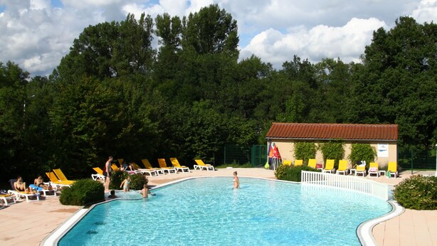Une piscine entourée d’une clôture et d’arbres, avec des chaises longues jaunes et blanches.