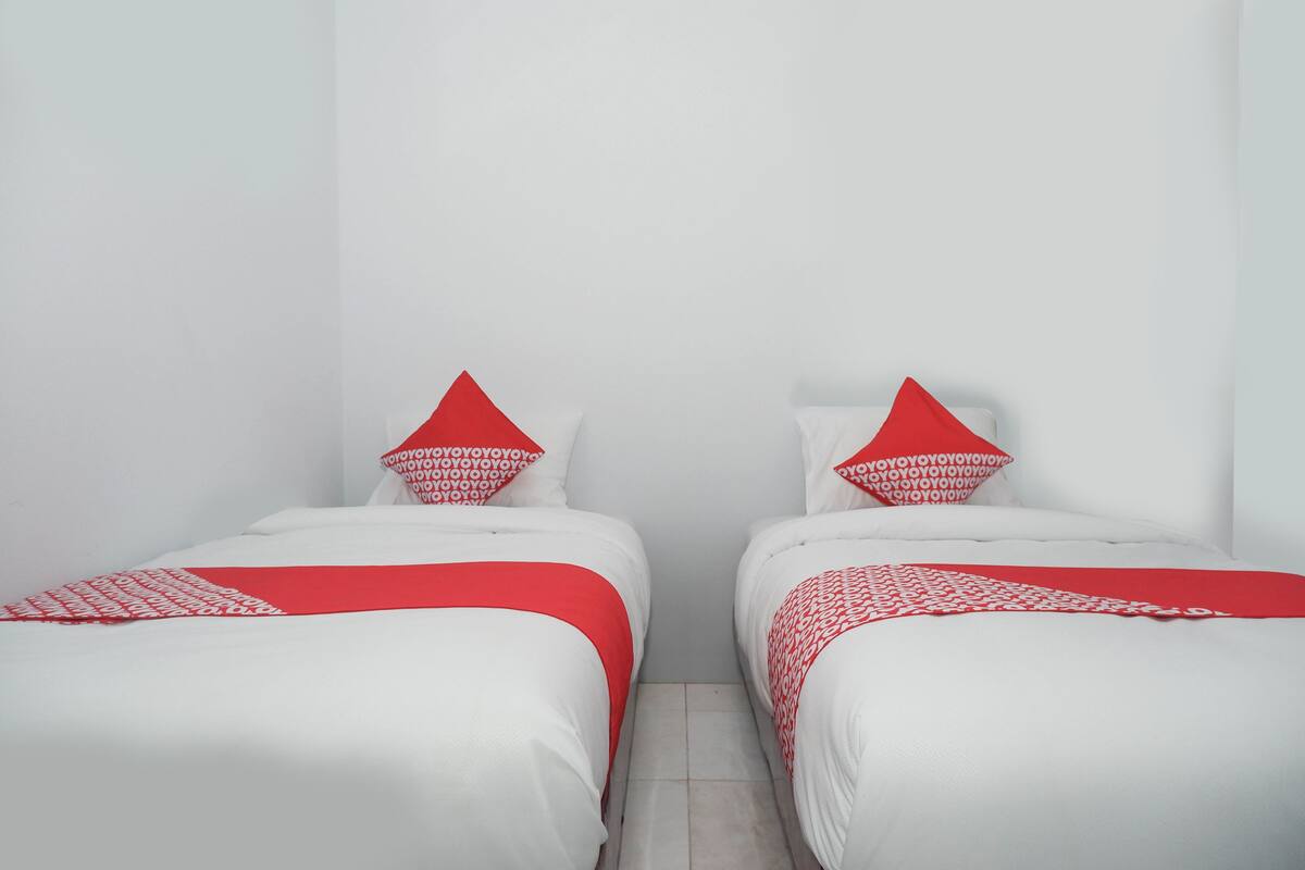 A room with two beds, each with white bedding and red pillows.