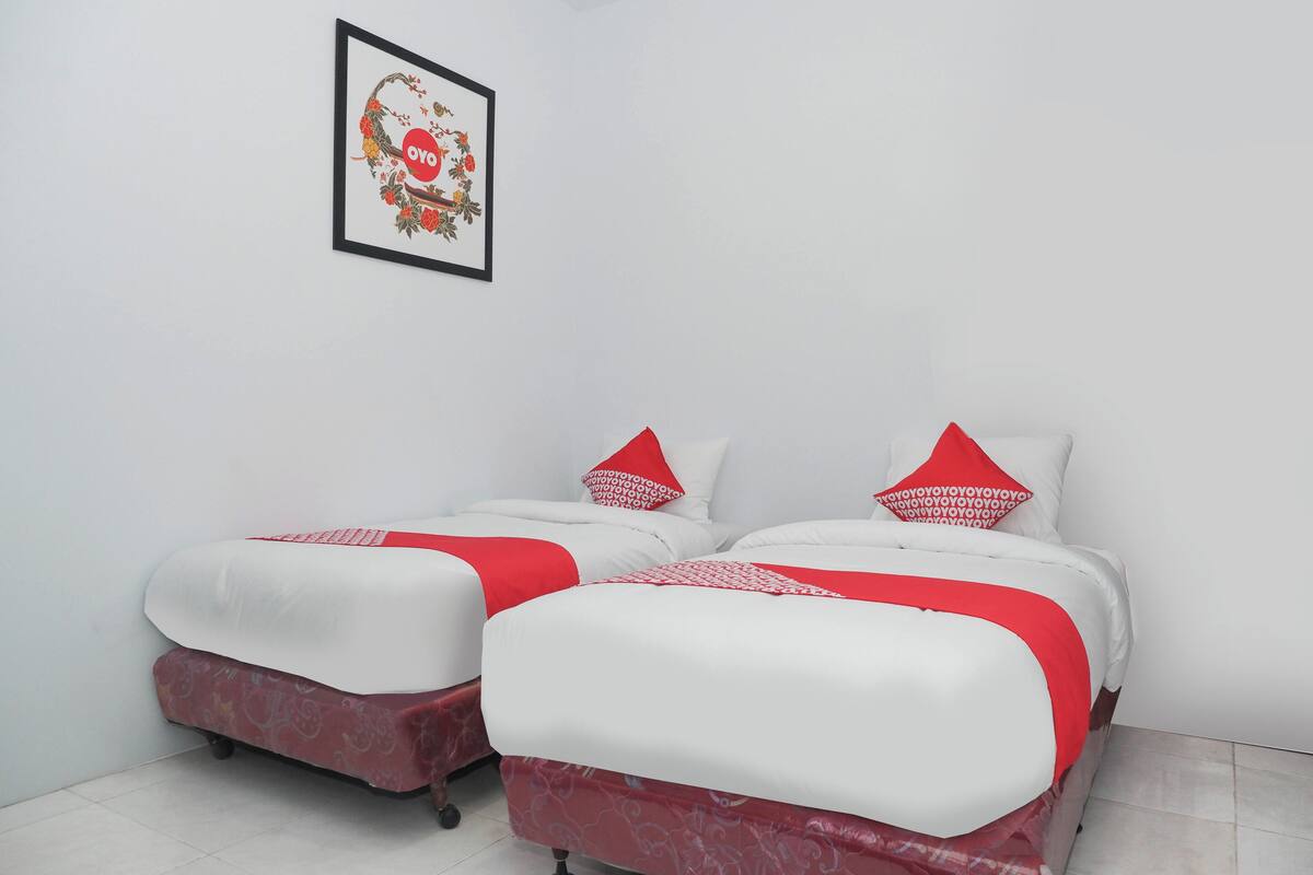A room with two beds, each with a red and white bedspread, a framed picture on the wall, and a tiled floor.