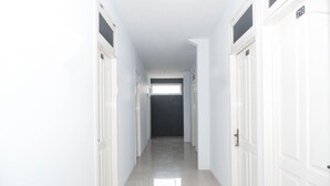 A long, narrow hallway with white doors on both sides, leading to a dark room at the end. - OYO 682 Ceria Homestay Syariah (Semarang)