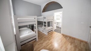 A room with bunk beds, a wooden floor, and a bathroom visible through an archway. - Factory Rooms Tarifa - Hostel (Tarifa)