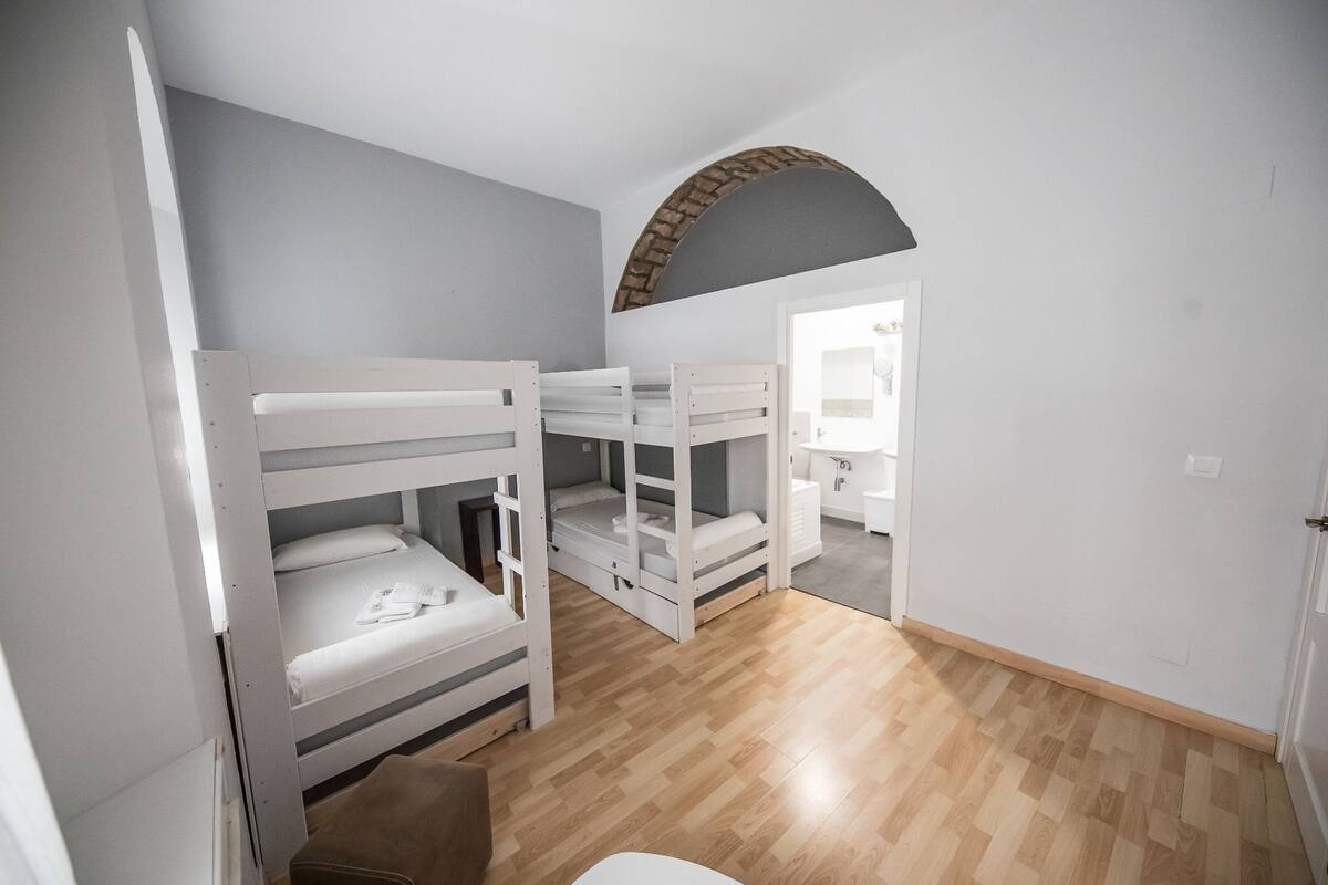 A room with bunk beds, a wooden floor, and a bathroom visible through an archway.