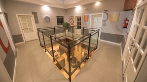 A spacious atrium with a glass railing, a clock, and a fire extinguisher on the wall. - Factory Rooms Tarifa - Hostel (Tarifa)