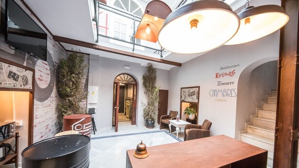 A modern hotel lobby with a reception desk, seating area, and a staircase. - Factory Rooms Tarifa - Hostel (Tarifa)