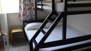 Une chambre avec un lit superposé, un petit tabouret et une fenêtre ornée de rideaux à motifs floraux.