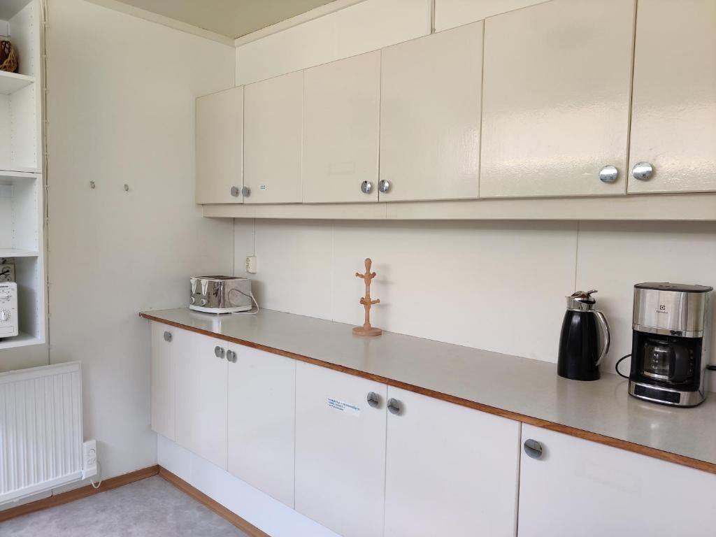 A kitchenette with white cabinets, a coffee maker, and a kettle.