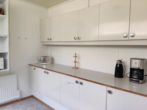 A kitchenette with white cabinets, a coffee maker, and a kettle. - Sólbrekka Guesthouse (Fjardabyggd)