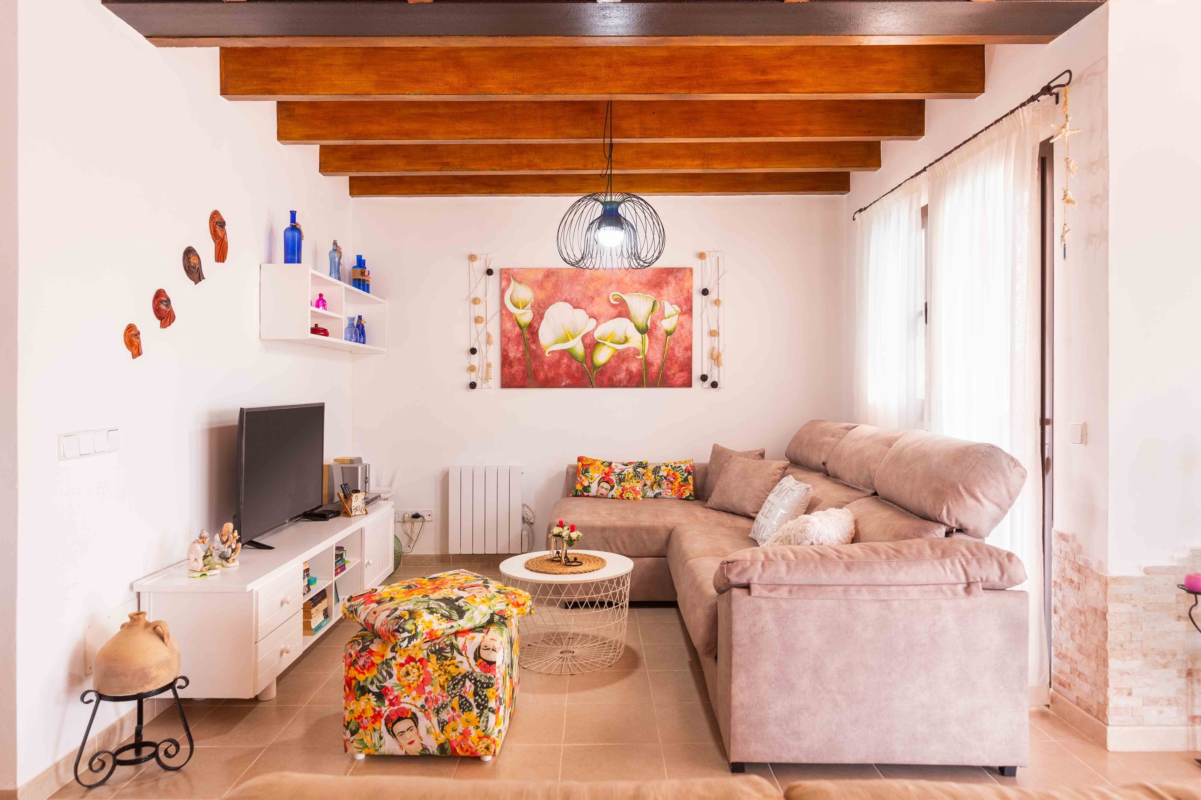 Un salon moderne avec un canapé, un pouf, un téléviseur et des œuvres d’art accrochées au mur.