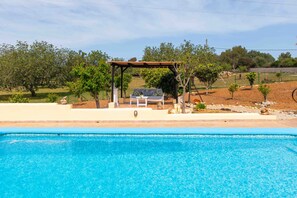 Une piscine agrémentée d’une pergola et de chaises longues, entourée d’arbres et d’un jardin aménagé.