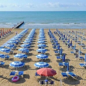 Una platja amb files de papereres i gandules blaves i vermelles.