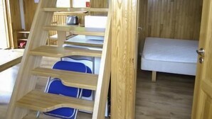 A wooden interior with a bunk bed, a desk, and a chair.