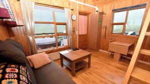 A wooden interior with a sofa, a table, a child's desk, and large windows.