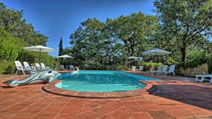 Ein Pool mit Whirlpool, umgeben von Liegestühlen und Sonnenschirmen, mit Bäumen im Hintergrund.