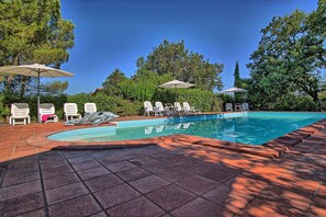 Une piscine entourée d’arbres, avec des chaises longues et des parasols.
