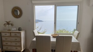 Een eethoek met een tafel, stoelen, een dressoir, een spiegel en uitzicht op zee.