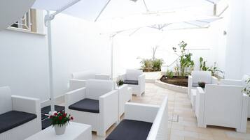 Un espace patio avec des meubles en osier blancs, un petit jardin et un mur blanc.