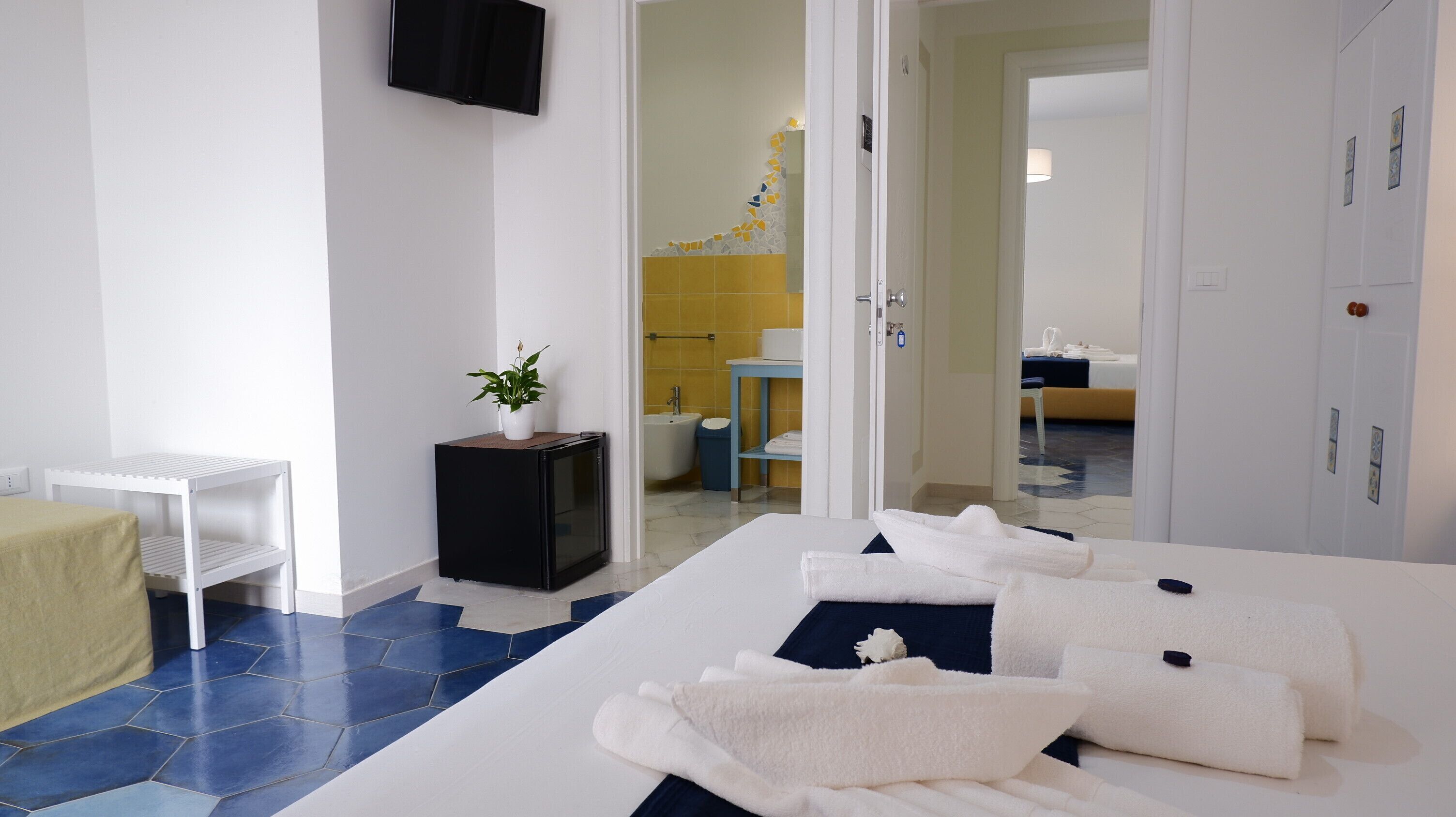Een hotelkamer met een bed, een klein tafeltje, een televisie en een badkamer zichtbaar door een geopende deur.