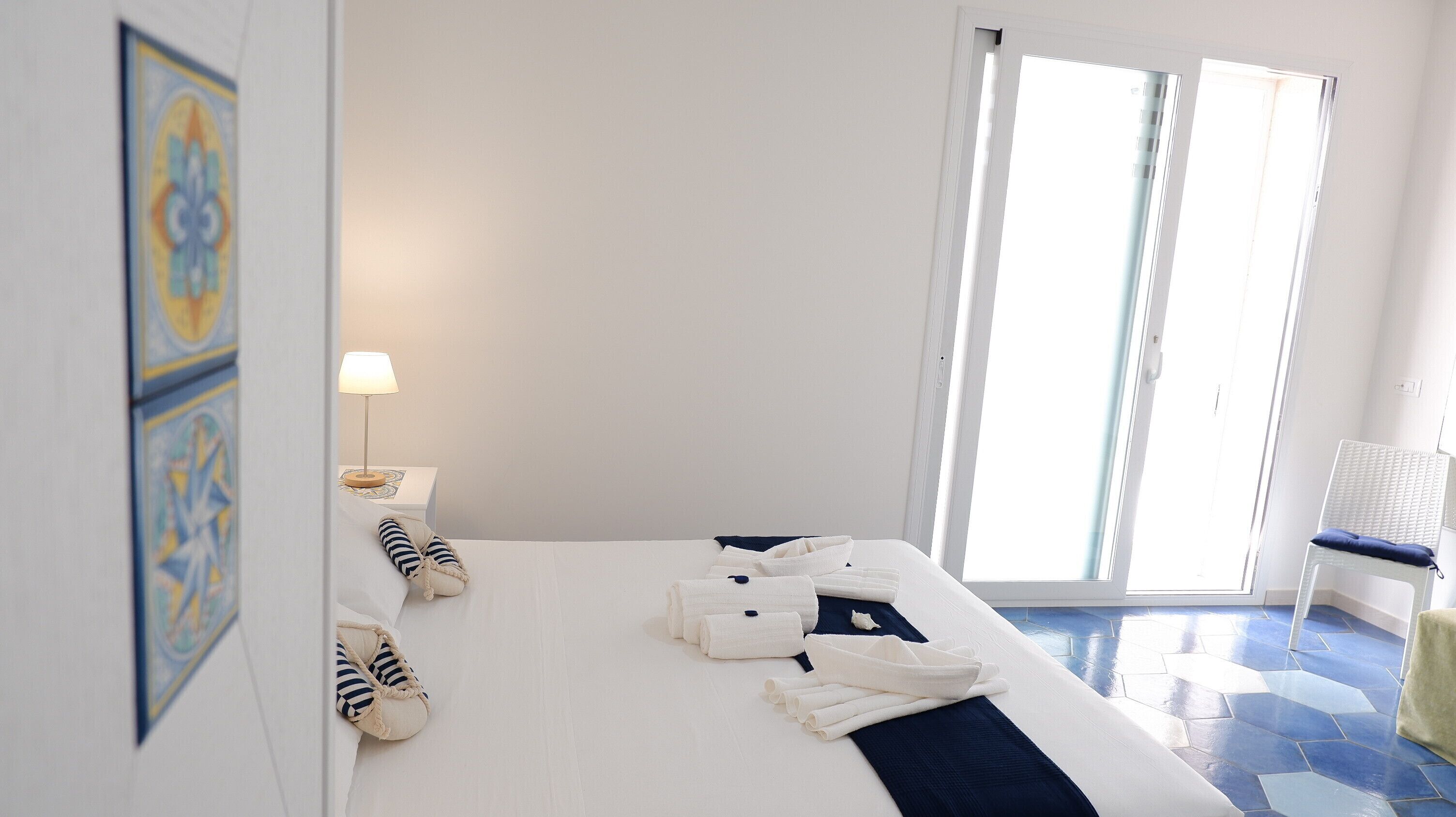 Ein Hotelzimmer mit Bett, Nachttisch, Lampe, Stuhl und Blick ins Freie.