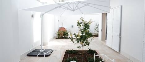 A clean, white interior courtyard with a small tree, a white table, and a white chair.