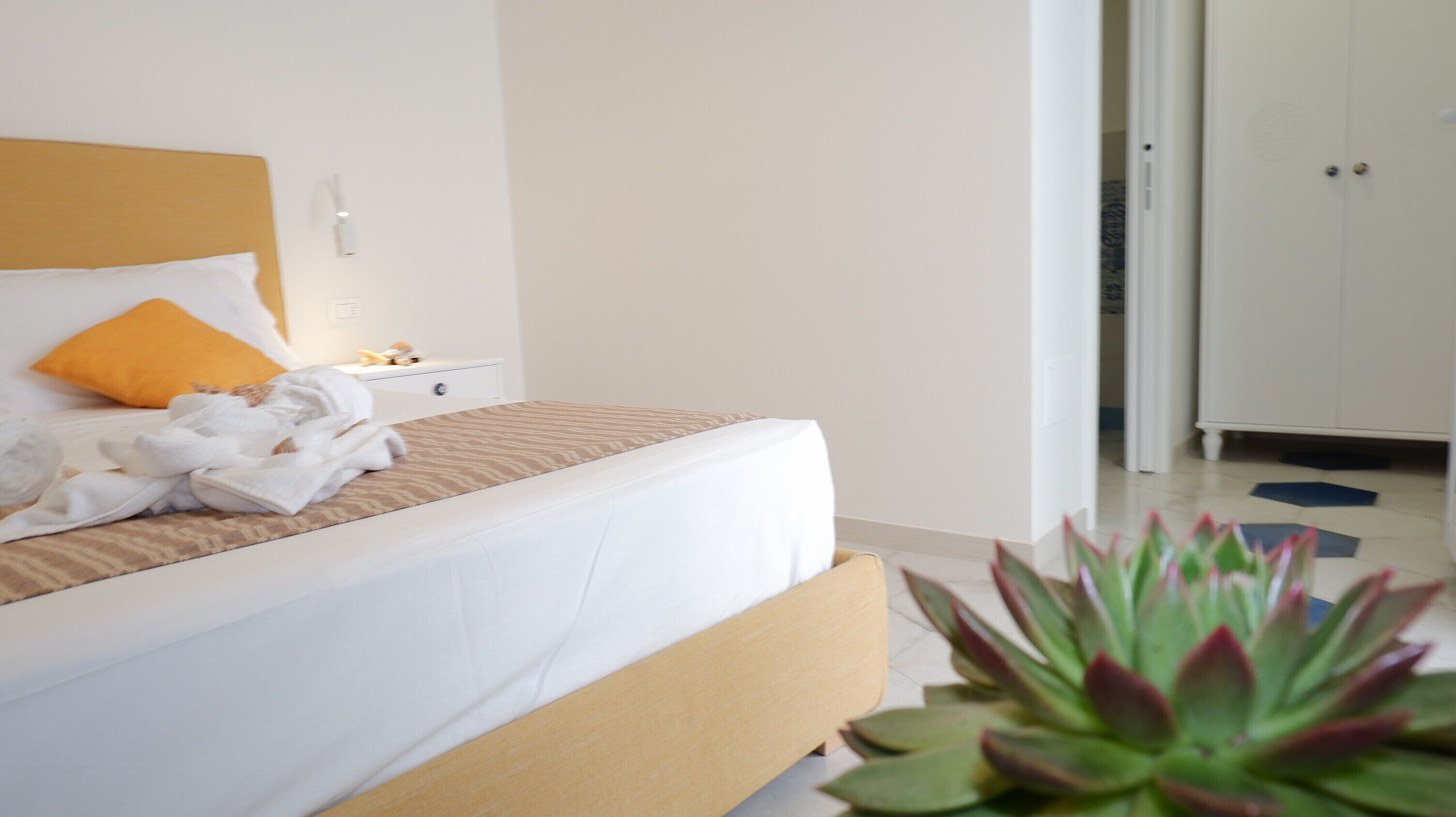 A hotel room with a bed, a nightstand, a lamp, and a potted plant.