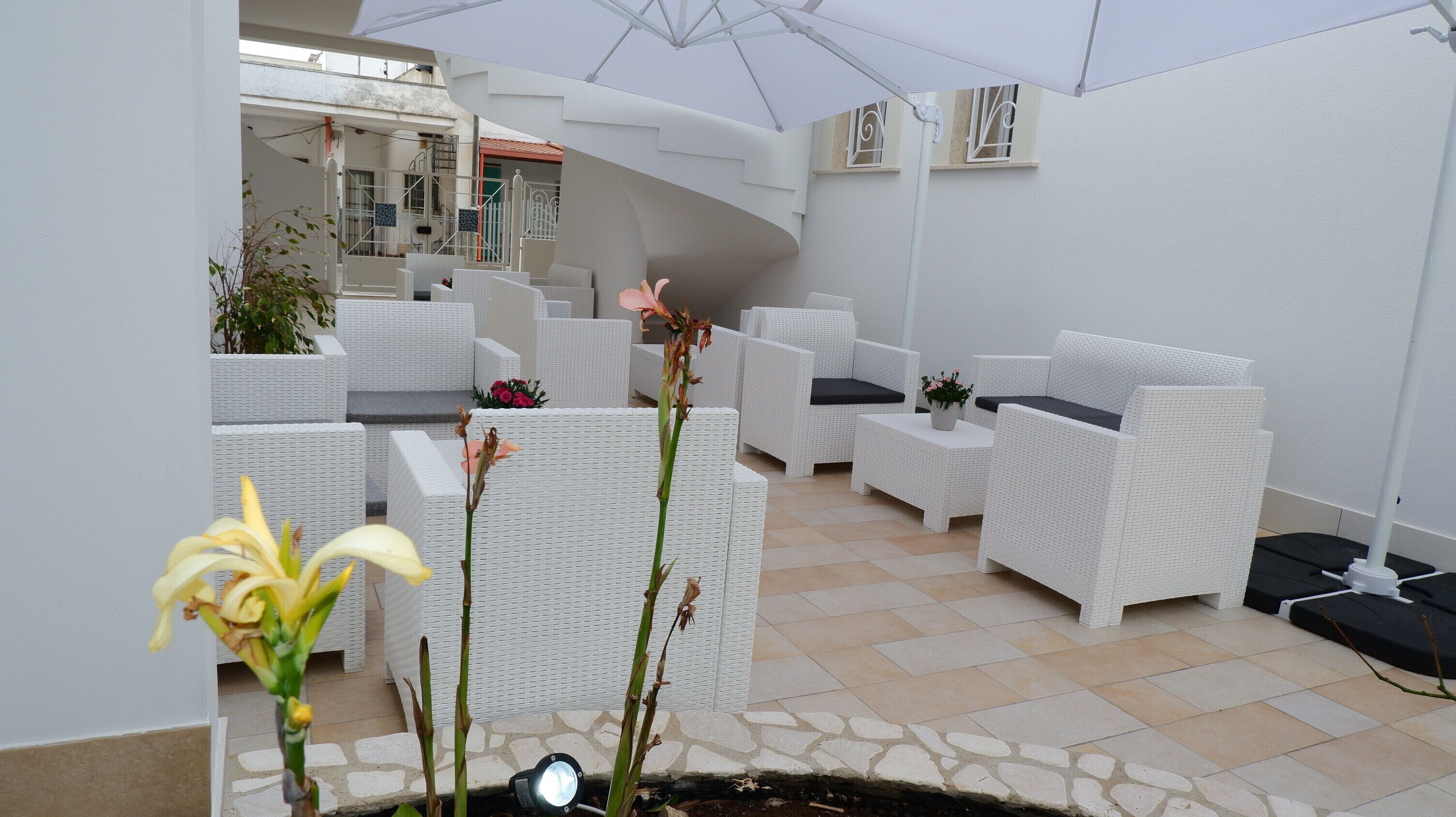 Un área de estar moderna al aire libre con mobiliario de mimbre blanco, suelo de piedra y un gran paraguas que da sombra.