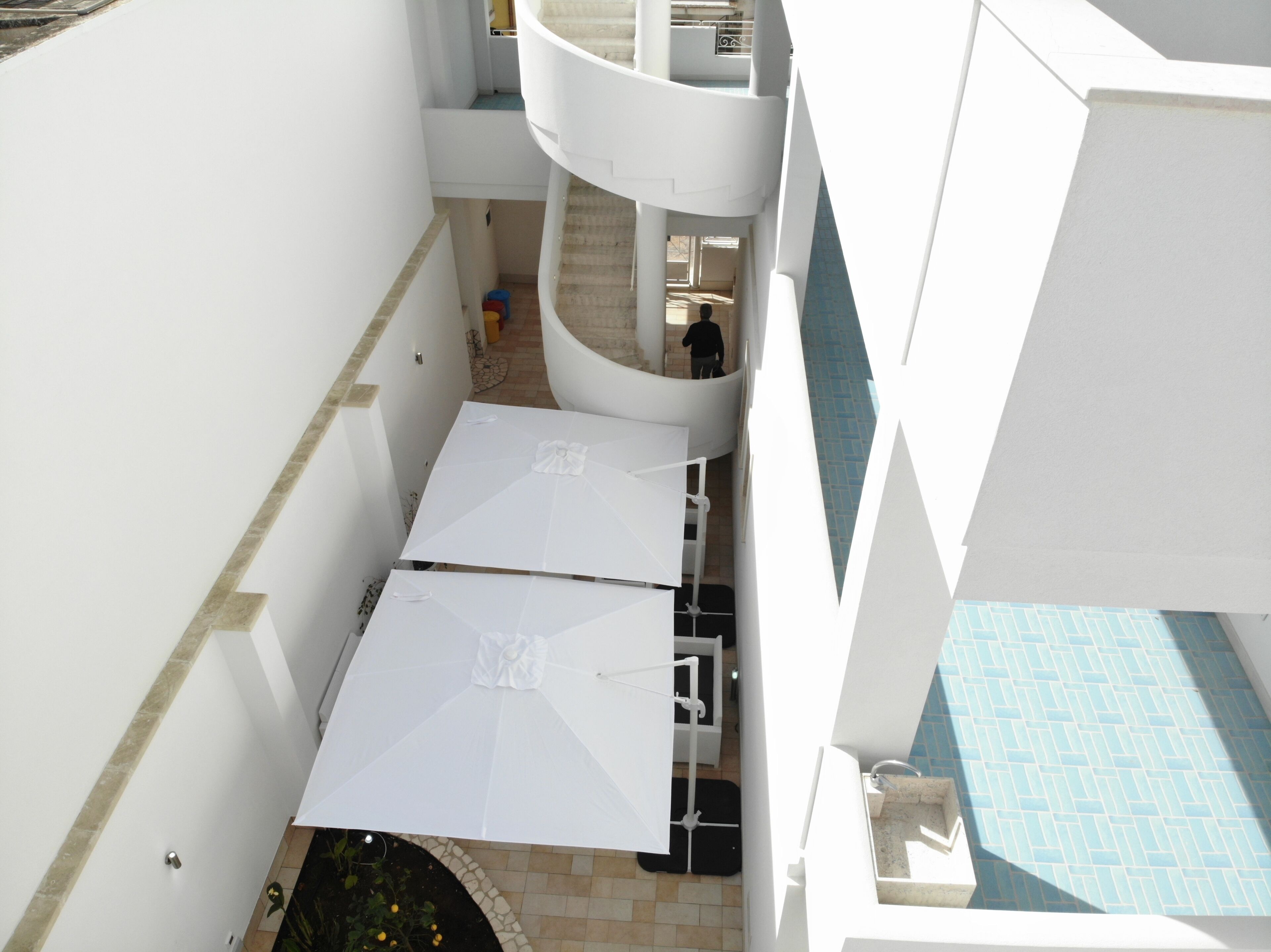 Un edificio de varios niveles con zona de piscina, sombrillas blancas y una escalera.