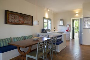 A modern kitchen with a dining area, featuring a wooden table, striped cushions, and a large decorative piece on the wall.