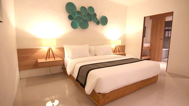 A modern bedroom with a large bed, two bedside tables, and a wall-mounted light fixture. - Anza d'Dimmel Jimbaran (Jimbaran)