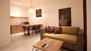 A compact living space with a sofa, a coffee table, a dining area with chairs, a kitchen counter, and a hanging light fixture. - Anza d'Dimmel Jimbaran (Jimbaran)