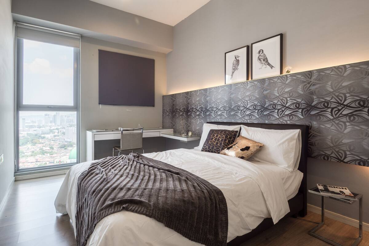 A modern bedroom with a large bed, a desk, and a city view.