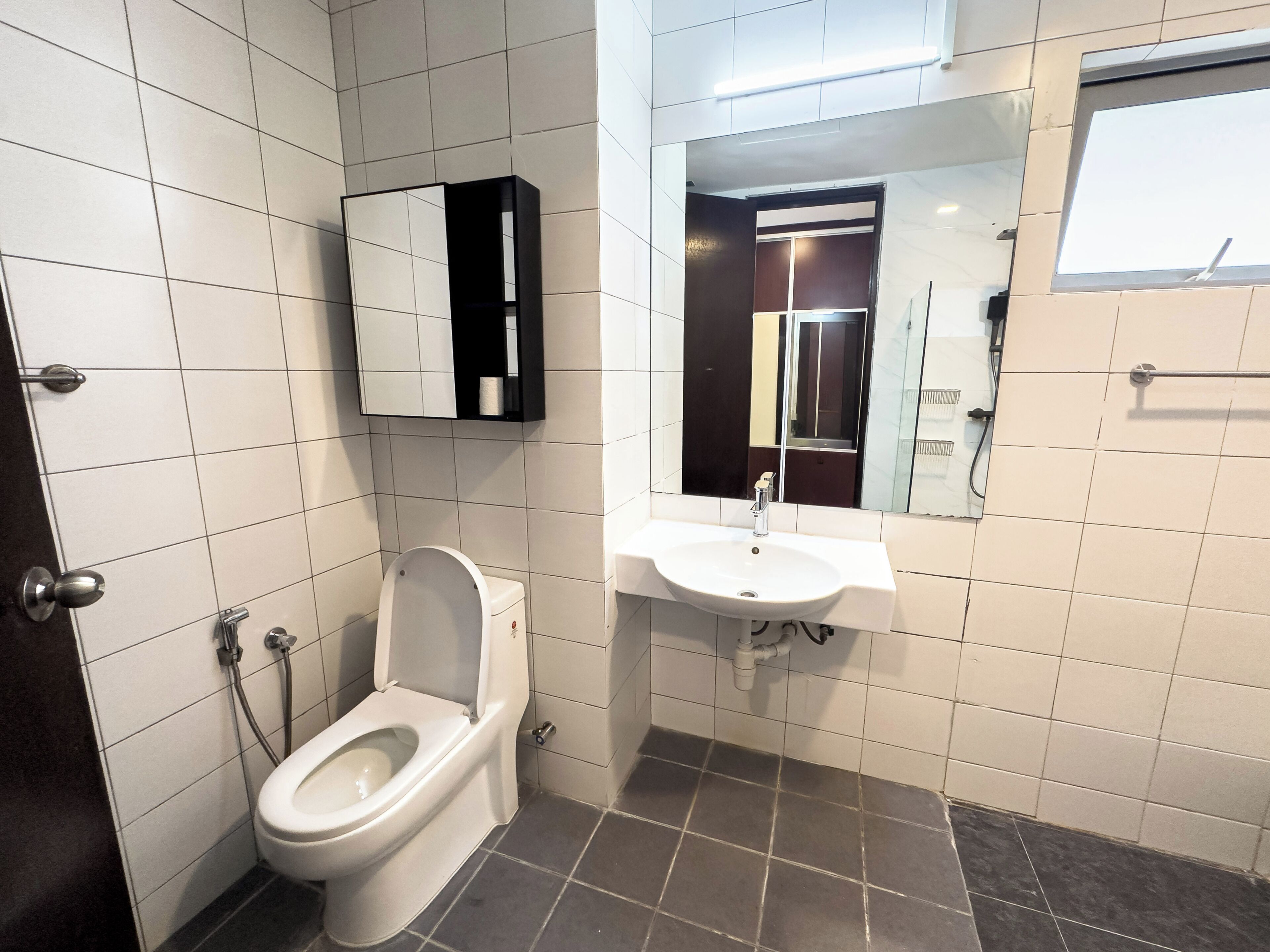 A bathroom with a toilet, sink, mirror, and tiled walls.