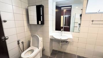 A bathroom with a toilet, sink, mirror, and tiled walls.