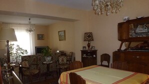 Un comedor con una mesa dispuesta para cuatro personas, rodeada de sillas estampadas. Un candelabro cuelga del techo y se ve una planta en maceta al fondo.