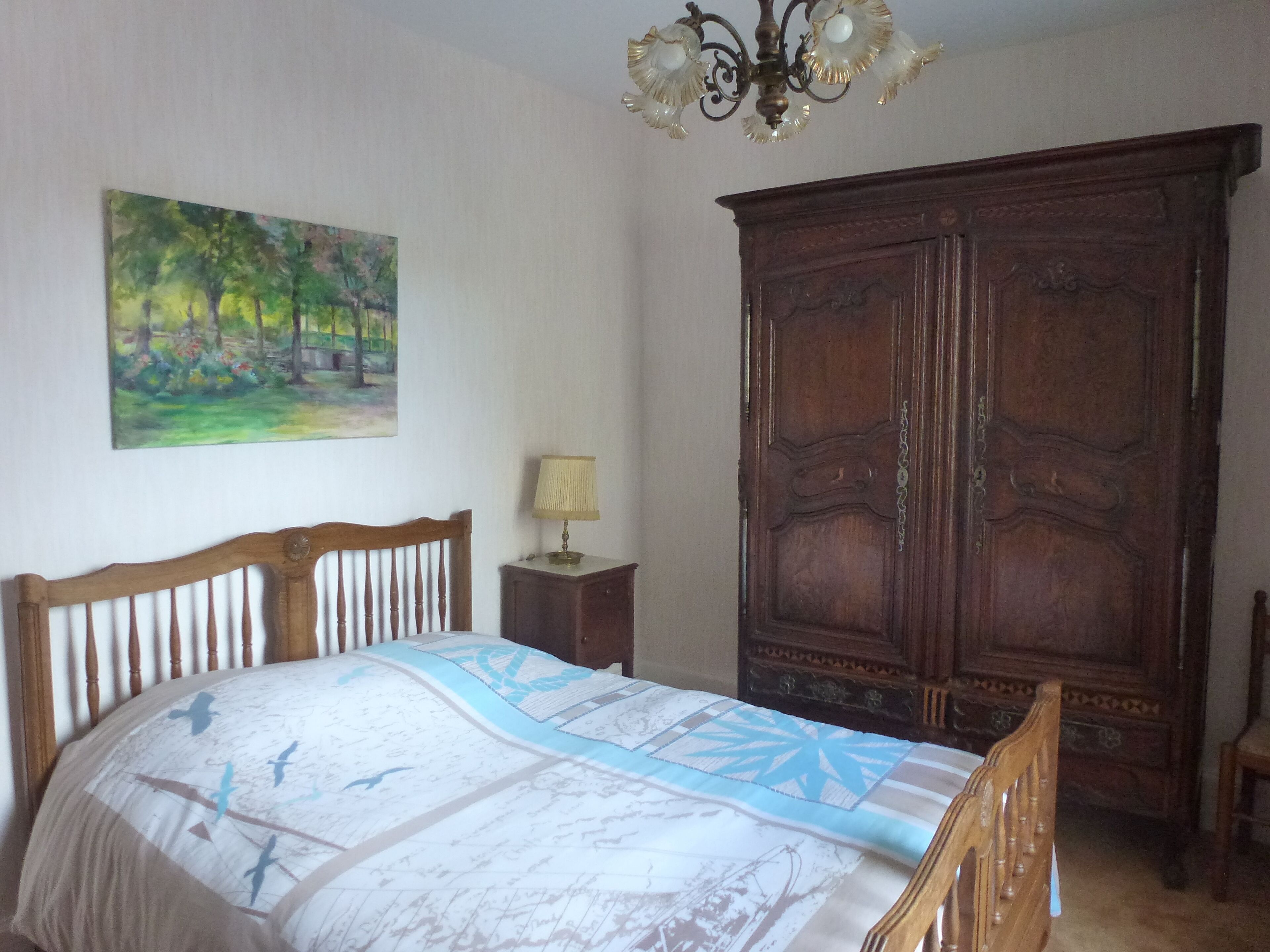 A bedroom with a wooden bed, a nightstand with a lamp, a large wardrobe, and a painting on the wall.