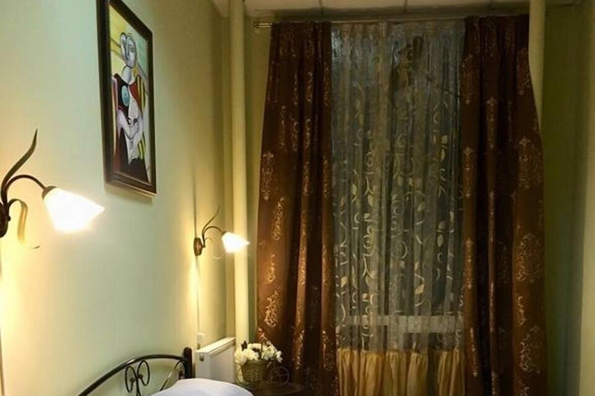 A bedroom with a single bed, a small round table, a wall-mounted lamp, and a painting.