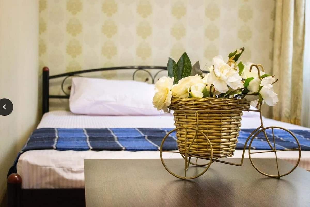 A bed with a blue and white striped bedspread, a white pillow, and a wicker basket with white flowers on a wooden table.